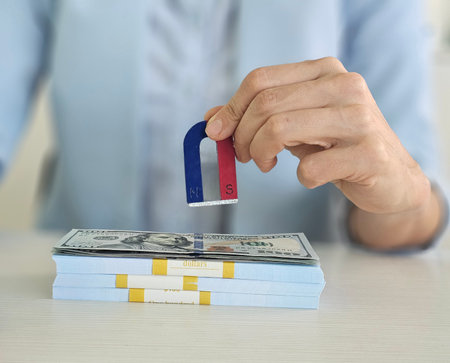 Businesswoman uses magnet to attract dollar bills during money management demonstration. wealth attraction investments and financial successの写真素材