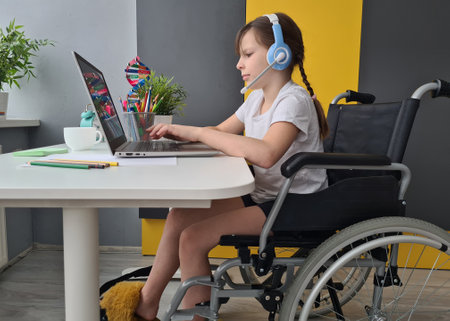 Young Girl Sitting in Wheelchair Using Laptopの写真素材