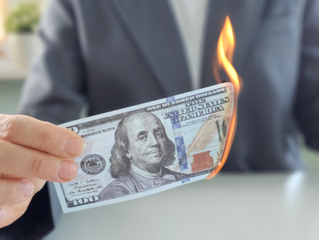 Money burning in a person's hand while wearing a suit with a blurred background in an indoor settingの写真素材