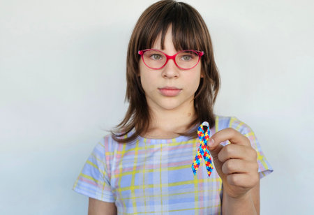 Girl holding colorful ribbon symbolizing autism awareness in a bright settingの写真素材