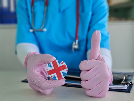 Medical professional displays a round pin with the UK flag and gives a positive thumbs up in a clinical settingの写真素材