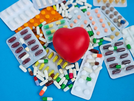 Health and wellness concept with colorful pills scattered around a red heart symbol on a blue backgroundの写真素材
