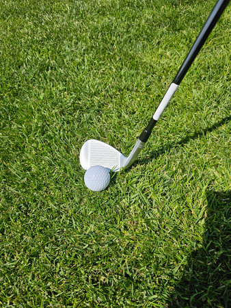 Golf club poised to strike a ball on well-maintained grass during a sunny afternoon on the golf