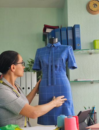 Tailor adjusting a blue dress on a mannequin in a bright workshop environment