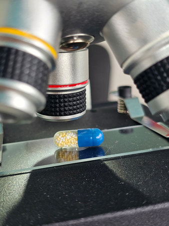 Closeup view of a blue and yellow capsule under a microscope lens in a lab setting showing casing...
