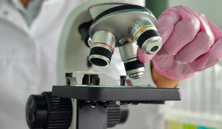 Scientist examines specimen under microscope in laboratory setting during daytimeの写真素材