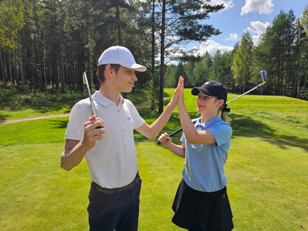 Golfers practicing swings in sunny weather at a green course surrounded by treesの写真素材