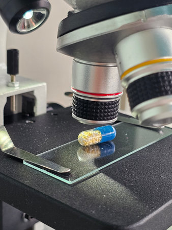 Close-up view of a blue and yellow capsule under a microscope in a laboratory setting during a research sessionの写真素材