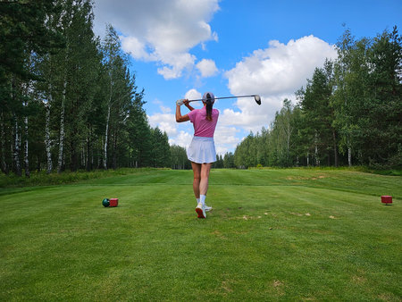 Golfer preparing to tee off in a lush green forested golf course under a partly cloudy skyの写真素材