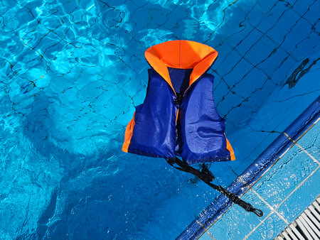 Brightly colored life jacket floating in clear pool water on a sunny day