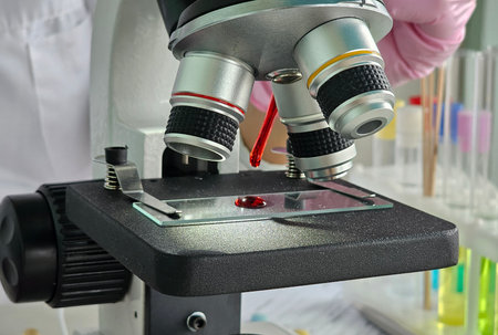 Laboratory microscope focused on slide with red sample in modern research environment
