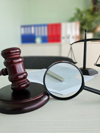 Gavel and magnifying glass on a desk with law books and scales in a legal office settingの写真素材