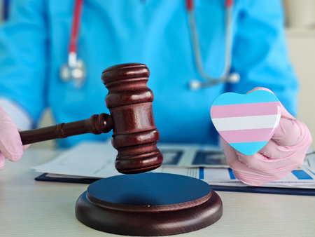 Medical professional holds heart symbol while gavel rests on desk in court setting focused on transgender rightsの写真素材