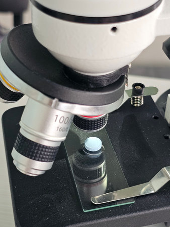 Close view of a microscope focusing on a glass slide with a specimen under examination for...