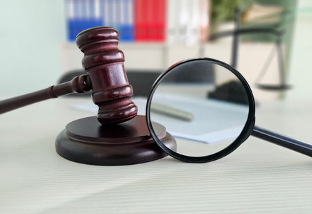 Gavel and magnifying glass on a desk in a legal office setting with documents and scales in the backgroundの写真素材