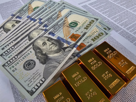 Wealth in dollars and gold bars displayed on financial news articles illustrating investment and luxuryの写真素材