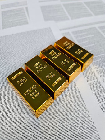 Gold bars stacked on newspaper with unique designs displayed indoorsの写真素材