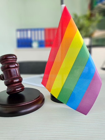 A small LGBT rainbow flag next to a wooden gavel on a table in a modern office.の写真素材