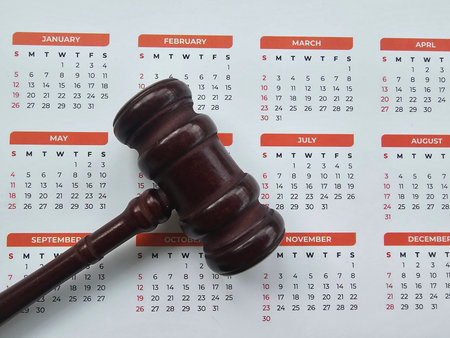 Wooden gavel placed on a calendar displaying months and days of the yearの写真素材