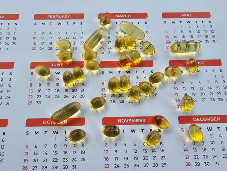 Assorted soft gel capsules scattered on a calendar highlighting different months and dates conceptの写真素材