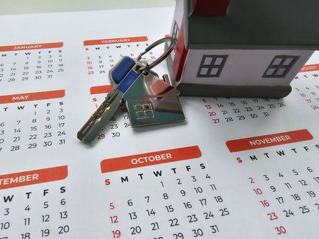 House keys placed next to a small house model on a calendar highlighting important datesの写真素材