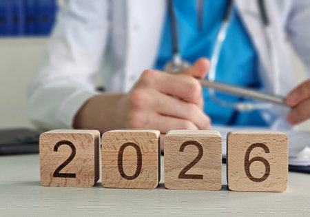 Doctor sits at a desk writing notes while wooden blocks display the year 202