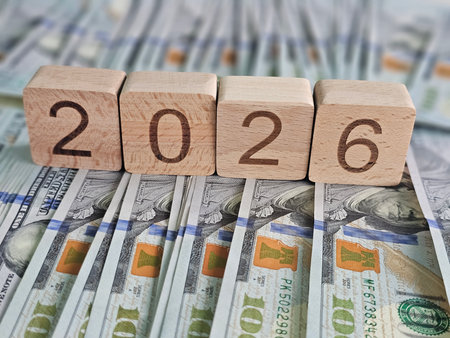 Wooden blocks show the year 2026 on a background of numerous hundred-dollar billsの写真素材