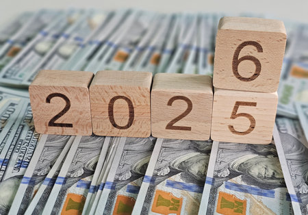 Blocks spelling out 2025 and 2026 are placed on top of a stack of hundred dollar bills illustrating...