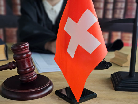Swiss flag displayed in a courtroom setting with a gavel and legal documents on the tableの写真素材