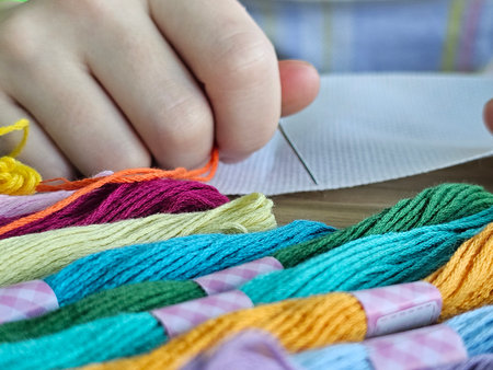 Hands threading a needle with colorful embroidery floss on a wooden table during a craft session