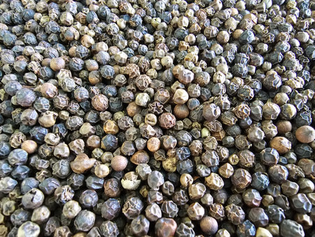 Black peppercorns drying under sunlight, showing their unique shapes and colors at a spice farm in...