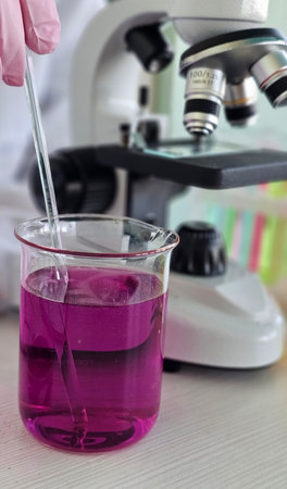 Scientist conducting an experiment with purple liquid under a microscope in a laboratory setting