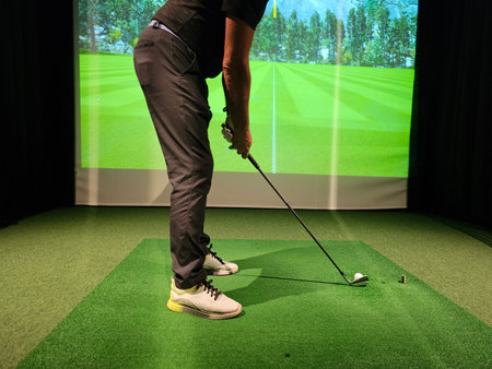 Golf player practicing swing at indoor simulator with realistic screenの写真素材