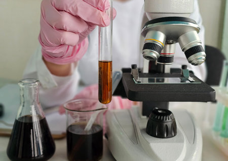 Laboratory technician examines liquid samples under microscope in a research facilityの写真素材