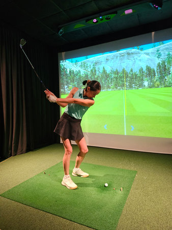Golfer practicing swings indoors at a virtual driving range on a sunny dayの写真素材