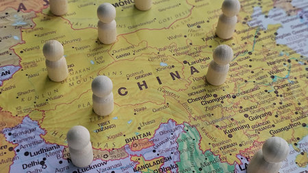 Wooden figures placed on a detailed map of China highlighting various cities and regionsの写真素材