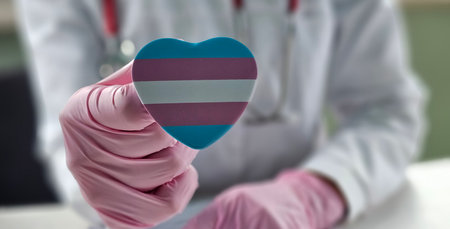 Healthcare professional holding a heart-shaped trans transgender pride symbol while discussing patient care during a consultationの写真素材