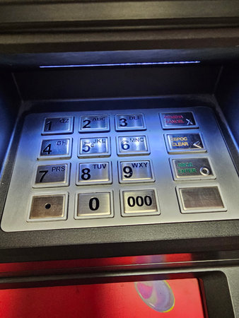 ATM keypad with bright lighting showing numbers and letters in an urban setting during daytime