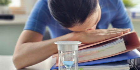 Students struggling with studies and time management while surrounded by books and an hourglassの写真素材