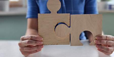 Hands holding two wooden puzzle pieces in a bright indoor space during daytime with natural lightの写真素材
