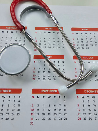 Calendar with stethoscope resting on it showing months and dates for planning appointments in a medical settingの写真素材
