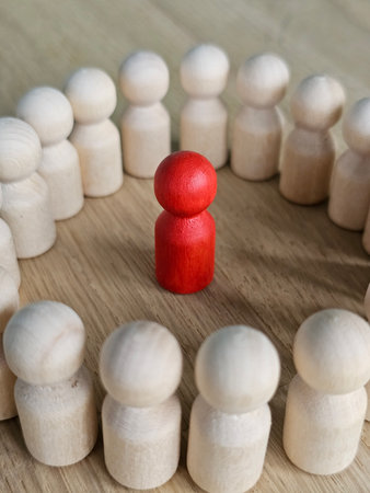 Red figure stands out in a circle of wooden figures symbolizing leadership and influence in a group settingの写真素材