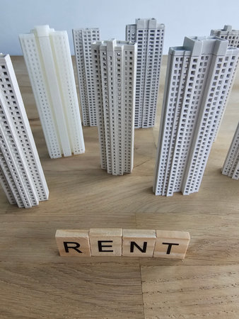 Small buildings made of plastic surround wooden blocks that spell rent on a tableの写真素材