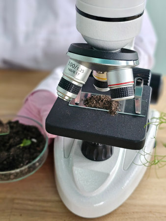 Scientist examines soil sample using microscope in laboratory setting during daytime