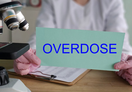 Medical professional holds a sign that says overdose next to a microscope in a lab setting during daytimeの写真素材