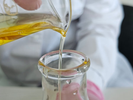 Oil is poured into a glass container by a person in a lab setting during a science experimentの写真素材