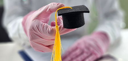 Small graduation cap held by a person wearing gloves in an academic settingの写真素材