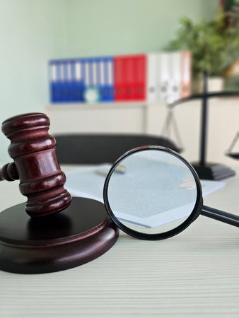 Court gavel and magnifying glass on a desk with documents and folders in an office settingの写真素材