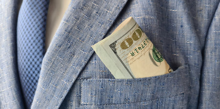 A man in a blue suit with a hundred-dollar bill peeking from the pocket during a professional...