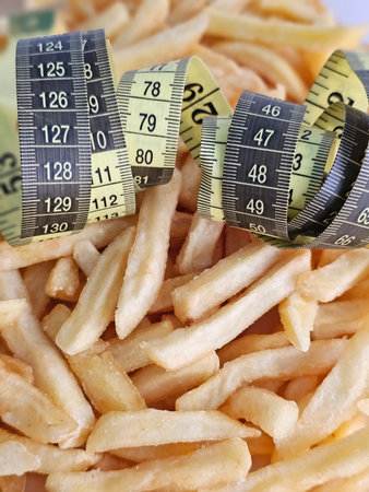 Measurement tapes wrapped around French fries on a plate convey a message about food and health...